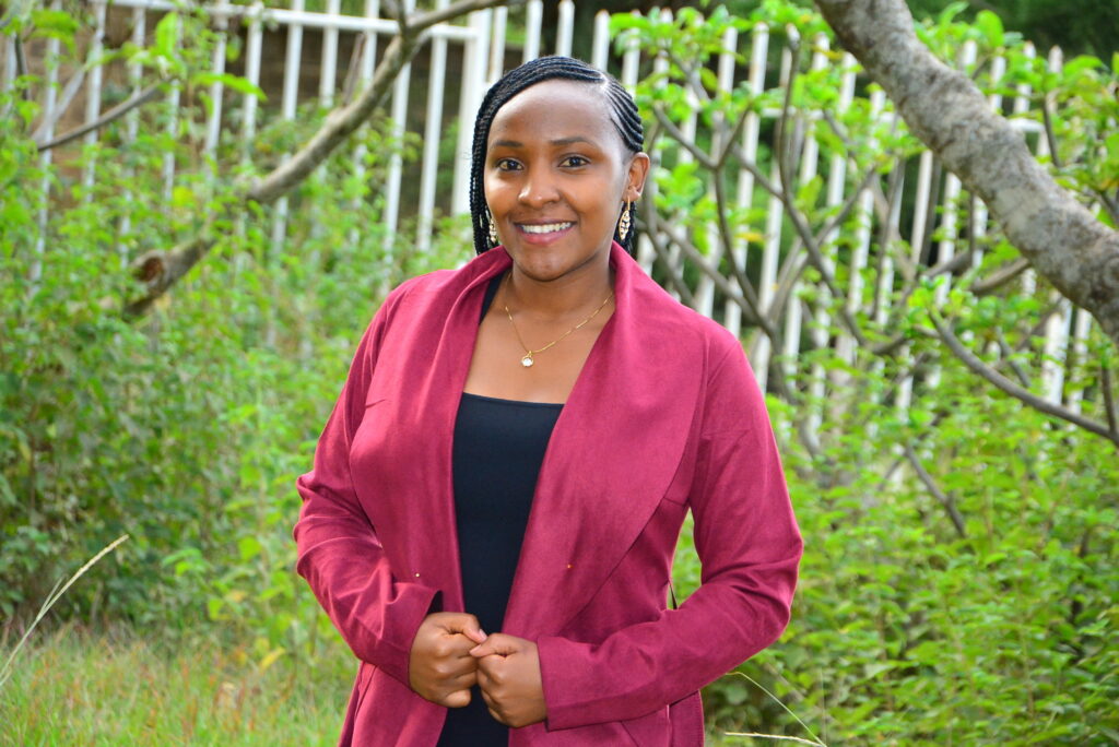 A young kenyan activist in a fuschia blazer with tress in the background